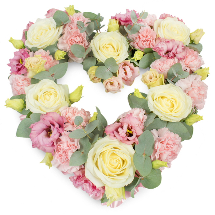 A beautifully composed, heart-shaped wreath is shown in full, its floral design rich with detail and crafted in the gentle tones often chosen for funeral and sympathy tributes in Purley. The heart is perfectly defined and densely filled so that flowers and greenery blend together into a continuous, full surface. Large, cream and pale yellow roses are placed evenly throughout the composition, their generous, velvety petals unfolding from tightly coiled centres. These roses create focal points that guide the gaze along the curve of the heart, evoking warmth, devotion, and quiet respect. Nestled among them, numerous pale pink carnations contribute a soft, textured layer; their frilled petals overlap like delicate fabric, creating a feeling of comfort and tenderness. Deeper pink and mauve lisianthus blossoms are woven in at intervals, their open, cup-shaped flowers adding subdued richness, a whisper of deeper emotion beneath the pastels. Silvery-green eucalyptus foliage threads naturally through the design, its round, slightly waxy leaves resting against petals, peeking from behind blooms, and subtly framing the heart's outline. Small yellow-green buds appear here and there, suggesting the continuity of life and memory. Against the clean white background, the interplay of colour-cream, blush, soft green, and touches of mauve-stands out clearly, allowing the viewer to picture both the texture and the gentle fragrance of fresh flowers. Created in the spirit of thoughtful local floristry, this heart-shaped wreath would feel at home at a Purley funeral service, crematorium ceremony, or memorial gathering, offering a graceful symbol of sympathy, love, and lasting remembrance.